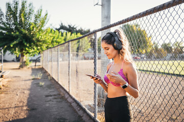 Young active woman using wireless headphones and setting a music playlist on her smartphone before work out