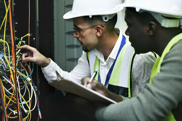 Detangling tech issues is what they do. Shot of two technicians working together in a sever room.