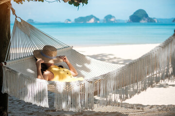 Happy Woman Traveler is relaxing in a hammock on the paradise beach. Female tourist in yellow dress rest near tropical sea. vacation, travel, summer, Wanderlust and holiday concept