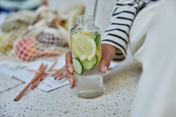 Cropped shot of unrecognizable woman holds bottle of fresh detox drink with lime and lemons rests outdoors after making drawings leads healthy lifestyle drinks organic beverage. Unknown person