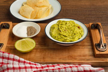 A bowl with fresh guacamole on a wooden tray over a wooden table