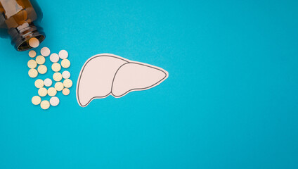 Top view of liver shape made from paper and pills capsules with a bottle on a blue background