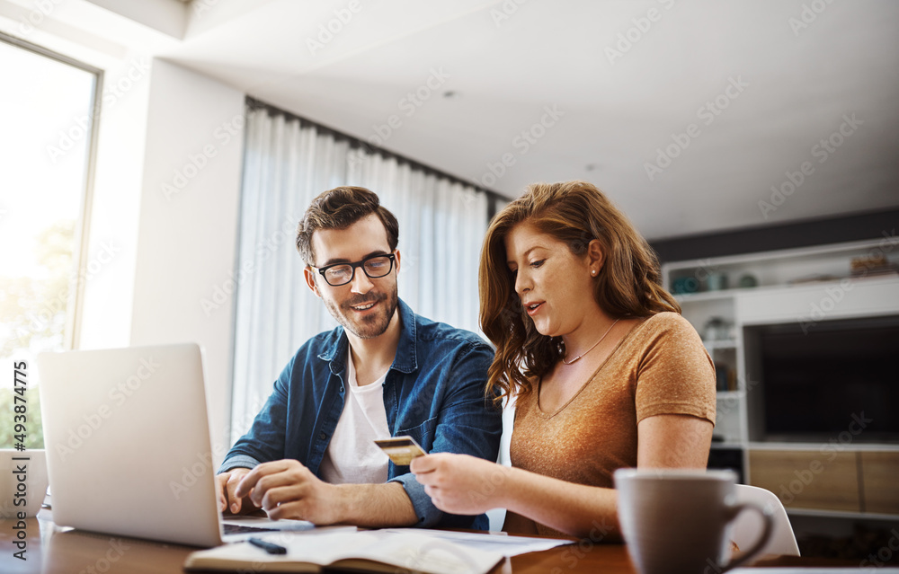 Poster Were spending wisely and maintaining a healthy budget. Shot of a young couple doing some online shopping on a laptop together over the weekend at home.