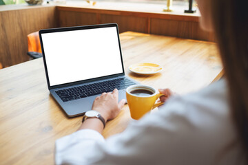 Mockup image of a woman using and working on laptop touchpad with blank white desktop screen while drinking coffee