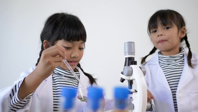 Two Asian siblings wearing coat are using the device for experimenting with liquids. They talking while studying science chemistry with fun