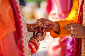 Tender hands of an Indian bride covered with henna tattoo hold groom's hand while he gives her a...