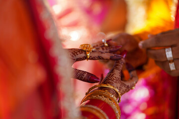 Tender hands of an Indian bride covered with henna tattoo hold groom's hand while he gives her a...