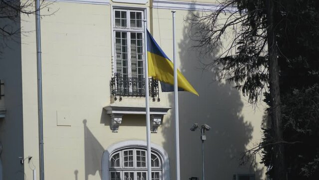 Ukraine flag blowing in the wind on a flag pole with an administrative building in the background