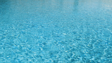 Bright blue water in swimming pool, motion surface in sunlight, close-up. Texture of clear turquoise water with small waves ripples, light reflection. Abstract azure liquid background
