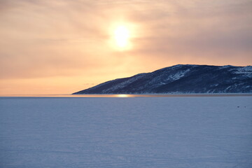 The setting sun over the icy river and the stone slope.