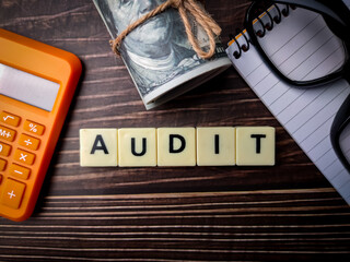 Top view calculator,banknotes,glasses and toys word with text AUDIT on wooden background.