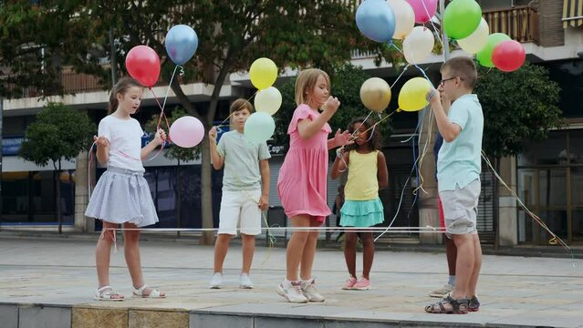 Kids playing with Chinese jumping rope outdoors. They're holding multicolored balloons in hands.