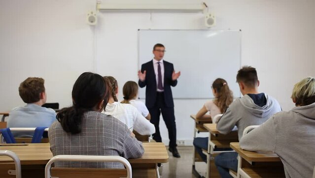 Portrait of professional male teacher giving lesson with interested teenagers in college