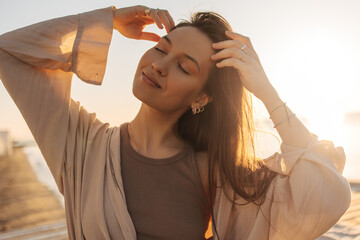 Close-up of young caucasian relaxed woman touching her hair in bright sunlight. Brown-haired girl...