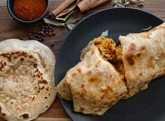 chicken salomie on black plate. Traditional roti and curry. Indian cuisine. Cape Malay cooking. Paratha flatbread and spices in the background. 