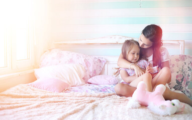 Young girl reads a book Young girl with a daughter are sitting on the bed. Summer house in the village by the garden. Rest of a young mother and daughter in the village.