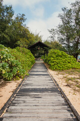 A wooden walkway next to the beach, with a wooden shade pavilion at the end