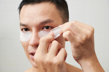 Face of young man applying hydrating undereye patches, morning routine concept