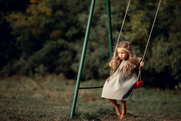 little cute sad girl swings barefoot on a swing on a spring day, summer. The concept of children's summer vacation, Family leisure and outdoor play concept. safety on the playground.