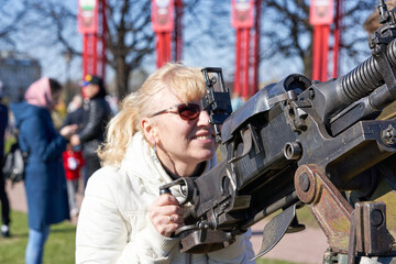 blonde woman in dark glasses shoots an anti-aircraft machine gun aiming upwards - 493887943