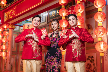 Fototapeta na wymiar two asian men A young woman wearing a red traditional Chinese cheongsam holds a red envelope and a lantern with Chinese text. written blessing It is a good luck blessing for Chinese New Year.