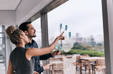 Envisioning the success they hope to achieve. Shot of two businesspeople brainstorming on a glass...