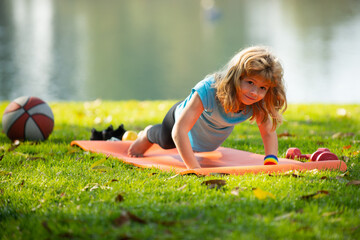 Child is pushing up on the green meadow, working out wearing sportswear, t-shirt outdoor. Kids doing push up outdoor. Gymnastic for children. Kid pushing up.