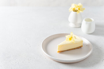 Classic New York cheesecake with fresh vanilla flower on white concrete background, side view. A piece of Vanilla cheesecake on a white plate. Confectionery menu, recipe. Copy space