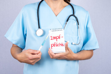 Eine Krankenschwester mit einer Spritze und einem Notizblock auf dem Impfpflicht steht