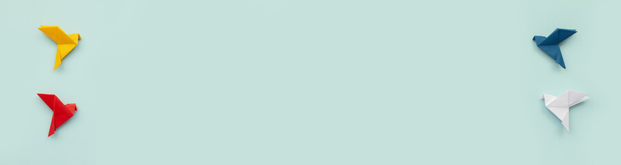 four paper origami pigeons red, blue, yellow and white on light blue background, banner