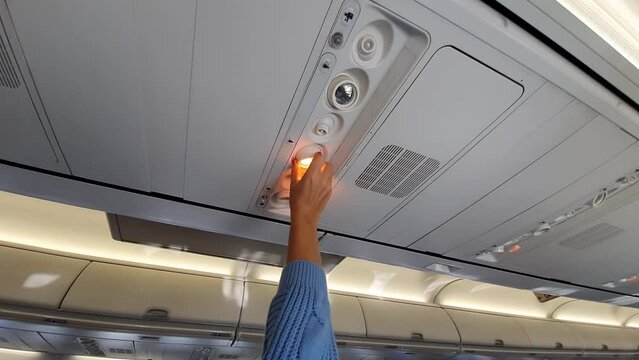 Girl adjusts the light in the plane cabin.