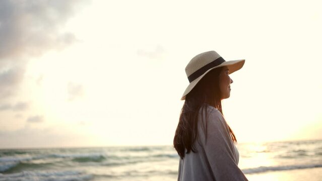 Side view young woman with hat walk into the sea with sunset moment. Happy female relaxing on vacation time holiday weekend after hard work all day. Travel and resting on the beach concept.
