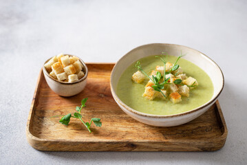 Bowl of broccoli cream soup with parmesan cheese, crunchy croutons and microgreen on a wooden tray,...