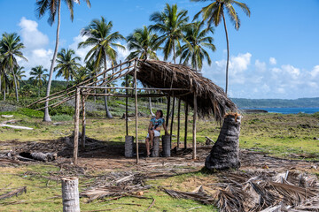 a woman in glasses and a hat close-up against the background of a wooden house in the local style in the Dominican Republic 