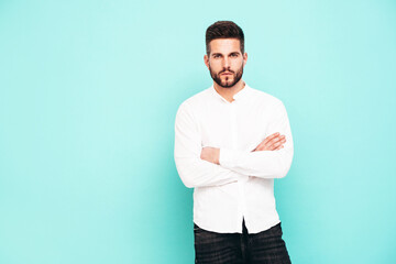 Portrait of handsome confident  model. Sexy stylish man dressed in white shirt and jeans. Fashion hipster male posing near blue wall in studio. Crossed arms. Isolated