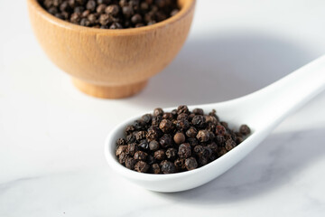 black peppercorns in a spoon on white