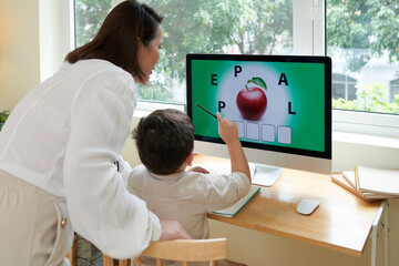 Mother helping son to solve puzzle on computer screen when he is studyig at home