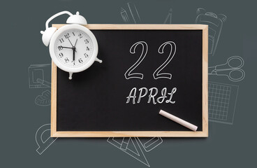 April 22. 22th day of month, calendar date.   Blackboard with piece of chalk and white alarm clock on green background. Concept of day of year, time planner, spring month