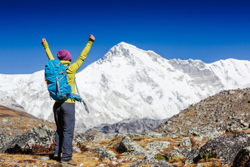 Obraz premium Female hiker cheering elated and blissful with arms raised in the sky after hiking in Himalayas