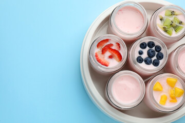Tasty yogurt in glass jars and ingredients on light blue background, flat lay. Space for text