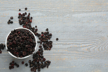 Fototapeta na wymiar Dried black currants and bowl on grey wooden table, flat lay. Space for text