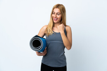 Young sport woman going to yoga classes while holding a mat over isolated white background celebrating a victory