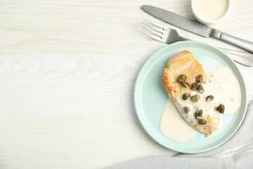 Delicious cooked chicken fillet with capers and sauce served on white wooden table, flat lay. Space for text