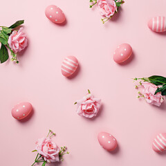Traditional table arrangement with color eggs and fresh roses on pastel pink background. Creative Easter holiday concept. Romantic springtime celebration pattern or texture. Flat lay.