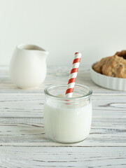 Glass of milk with red and white straw, cookies with chocolate, pitcher