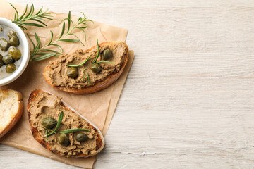 Slices of bread with delicious pate, capers and rosemary on white wooden table, flat lay. Space for...
