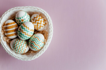 Colorful Easter eggs in a white basket on a pink background.