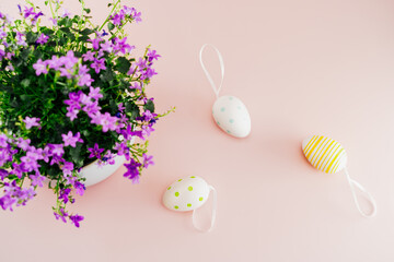 Top view bunch of spring purple flowers in the pot and painted Easter eggs decor on the light pink background. Flat Lay festive background. Selective focus. Copy space
