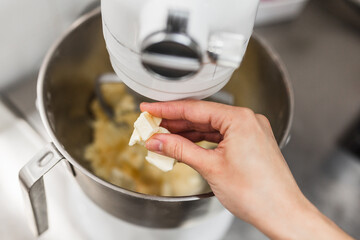 Close-up view of a hand of woman putting butter into a mixer