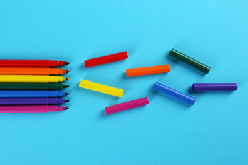 Fototapeta premium Many colorful markers on light blue background, flat lay. School stationery